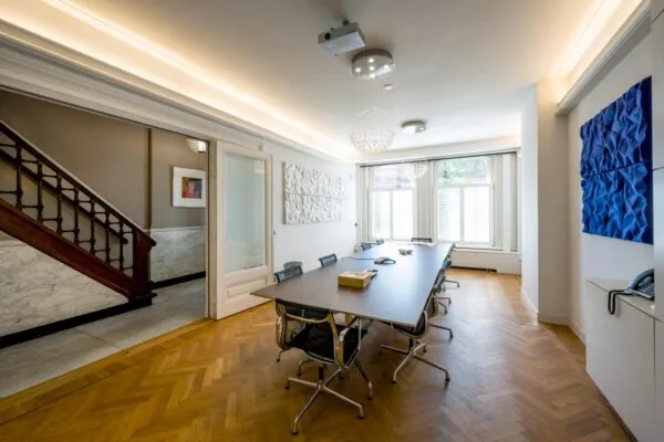 Vergaderruimte aan de Paulus Potterstraat met een lange tafel, moderne stoelen, kunst aan de muur en grote ramen met witte jaloezieën.